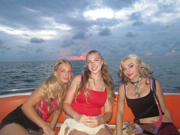 Three friends enjoy a sunset boat ride, capturing a moment of joy and camaraderie on the water.