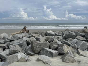 A rocky shoreline scene with a view of the ocean and cloudy sky, creating a serene coastal atmosphere.