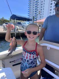 A young girl proudly holds up her catch while fishing on a boat, showcasing a joyful moment of family fun on the water.