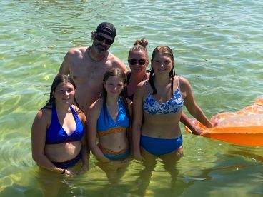 A joyful family poses together in shallow water, enjoying a sunny day at the beach — perfect for creating lasting memories during summer vacations.