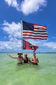 A joyful family poses in shallow water at the beach, celebrating under the vibrant flags — a perfect moment for summer fun and family bonding.