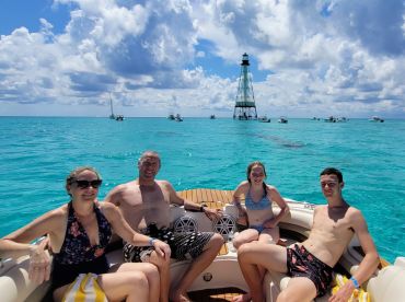 A cheerful family enjoys a sunny day on the water, relaxing on their boat with a lighthouse in the background — perfect for memorable boating adventures.