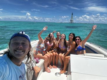 A joyful group of friends enjoys a sunny day on the water, capturing memories with smiles and waves aboard their boat — perfect for summer adventures.