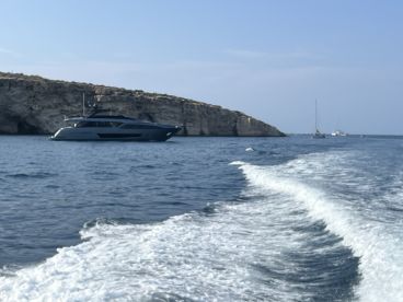 A sleek yacht navigates the waters near a rocky coastline, showcasing the beauty of boating adventures in serene surroundings.