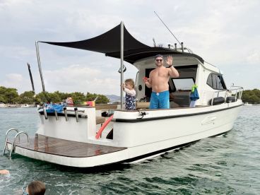 A family enjoys a fun day on the water, with a child playing near the boat while an adult waves from the deck — perfect for memorable summer outings.