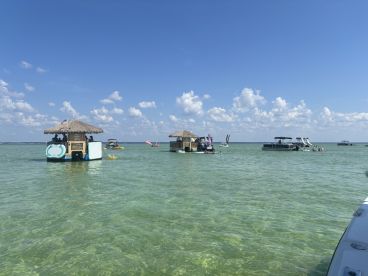 A vibrant scene at a sandbar with multiple boats and guests enjoying the water, perfect for a fun day of swimming and relaxation.