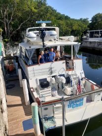 A cheerful group poses on the deck of their boat, 'License to Chill,' docked in a serene setting — perfect for memorable outings and adventures on the water.