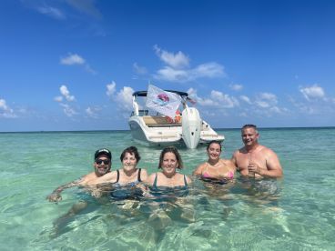 A cheerful group enjoys a refreshing swim in crystal-clear waters with their boat anchored nearby, perfect for a fun day at the beach.