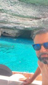 A person enjoys a scenic view of a cave with stunning turquoise waters, capturing the moment with a selfie — perfect for adventure seekers exploring hidden gems.