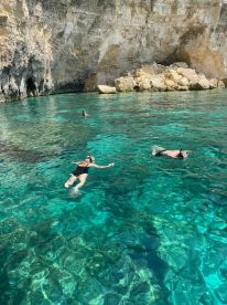 A group enjoys snorkeling in crystal-clear waters, surrounded by stunning cliffs — a perfect adventure for water enthusiasts.