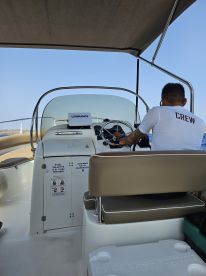 A view of the helm area inside a boat, showcasing the steering console and seating, with a crew member at the wheel, perfect for navigating the open waters.