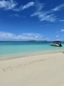 A stunning view of a boat anchored near a pristine beach in the Bahamas, with 'Bahamas' written in the sand — a perfect tropical getaway scene.