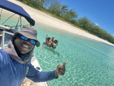 A joyful group enjoys a sunny day at the beach, swimming in crystal-clear waters while capturing the moment with a selfie — perfect for memorable outings and adventures.