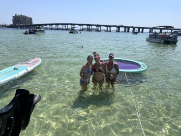 A fun group of friends enjoys a sunny day at the sandbar, swimming and relaxing in the shallow waters with a floating mat — perfect for summer parties on the water.