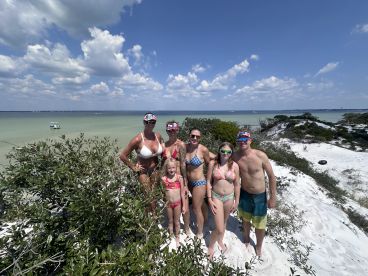 A cheerful family poses for a photo on a sandy beach, enjoying a sunny day by the water — perfect for memorable summer outings.