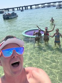 A lively group enjoys a fun day in the water, celebrating with drinks and laughter near a pontoon boat — the perfect summer getaway.