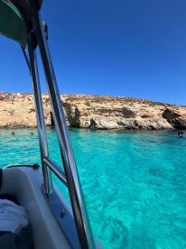 A picturesque view from a boat showcasing the stunning turquoise waters and rocky coastline, with people enjoying swimming nearby — a perfect destination for a summer getaway.