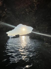 A stunning view from inside a cave, capturing the sun setting over the coastline — a perfect moment for nature lovers and adventure seekers.