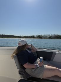 A guest enjoys a refreshing drink while relaxing on the boat, soaking in the sunny day and beautiful water views — perfect for a leisurely outing.