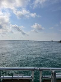 A serene view from the deck of a boat, showcasing calm waters and a distant lighthouse under a partly cloudy sky — perfect for a peaceful day on the water.