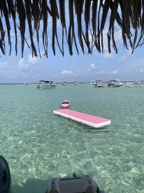 A vibrant scene showcasing multiple boats anchored in crystal-clear waters, with a floating mat inviting guests to enjoy the sun and fun — perfect for a day of relaxation and water activities.