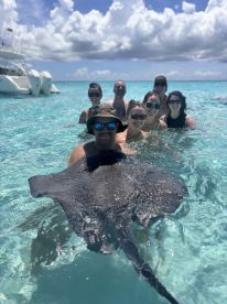 A group of friends enjoys a memorable experience swimming with a stingray in crystal-clear waters, showcasing the beauty of marine wildlife interactions.