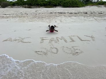 A child poses on the beach next to sand art that reads 'ABC FAMILY 2025' — a memorable moment capturing family fun in a tropical paradise.
