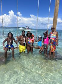 A joyful family enjoys a day at the beach, swinging in shallow waters with a boat in the background — perfect for creating lasting memories on summer vacations.