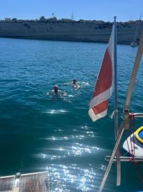 Two swimmers enjoy a refreshing dip in the clear blue waters, with a boat in the foreground, capturing the essence of a perfect day on the water.