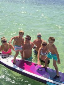 A joyful family poses on a paddleboard in clear waters, capturing a fun day of swimming and bonding under the sun.