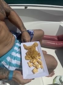 A man enjoys a plate of snacks featuring chips and cheese while relaxing on a boat, perfect for a day out on the water.