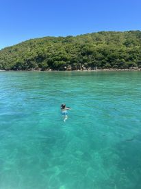 A child enjoys swimming in the crystal-clear waters near a lush island, showcasing the beauty of tropical destinations perfect for family adventures.
