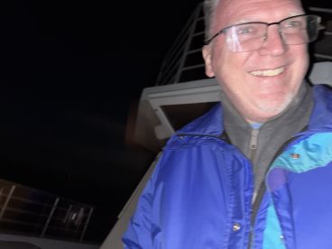 A blurry image of a person smiling on a boat at night, with limited visibility of the surroundings.