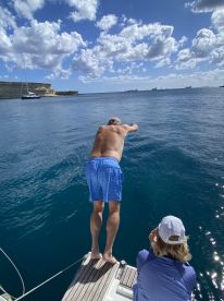 A man prepares to jump into the clear blue waters while a woman captures the moment aboard a boat, showcasing the fun and excitement of a day on the water.