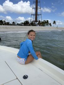 A young girl enjoys a sunny day on the boat, with a beautiful beach backdrop — perfect for family outings and water adventures.
