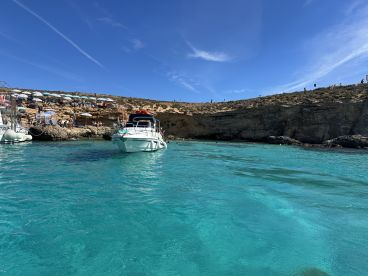A speedboat is anchored in stunning turquoise waters, surrounded by a scenic rocky coastline and beach umbrellas, perfect for a day of relaxation and exploration.