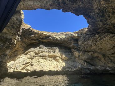 A stunning view of a natural cave with a hole in the ceiling, showcasing the beautiful blue sky above — a perfect destination for boat tours and exploration.
