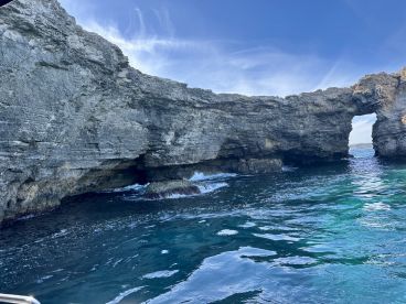 A stunning view of a natural rock arch along the coastline, showcasing the beauty of the surrounding waters — perfect for eco tours and sightseeing adventures.