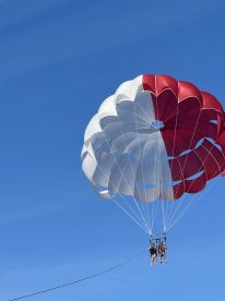 A couple enjoys an exhilarating parasailing adventure high above the water, surrounded by a clear blue sky — a perfect way to experience breathtaking views.