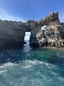 A stunning view of a natural rock arch along the coastline, showcasing the beauty of the surrounding waters — perfect for scenic boat tours and exploration.