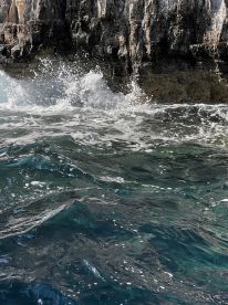 An unclear image capturing waves crashing against rocky cliffs, creating a dynamic seascape.