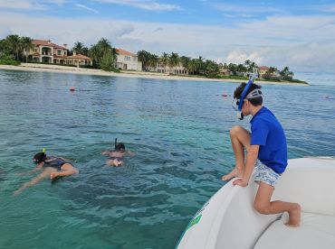 A group of kids enjoys snorkeling in clear waters, with one child preparing to jump from the boat — a perfect family adventure in a tropical paradise.