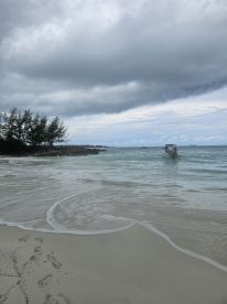 A serene view of a boat approaching a sandy beach under a cloudy sky, showcasing the tranquil beauty of coastal landscapes.