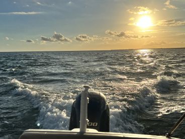 A stunning sunset view from the back of a boat, showcasing the shimmering water and tranquil atmosphere — perfect for evening cruises.