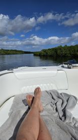 A serene moment on a boat, showcasing a person's feet resting on the deck while enjoying the tranquil waterway and lush greenery — perfect for relaxation and scenic views.