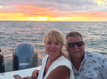 A couple enjoys a romantic sunset on the water, capturing a perfect moment together against a vibrant sky.