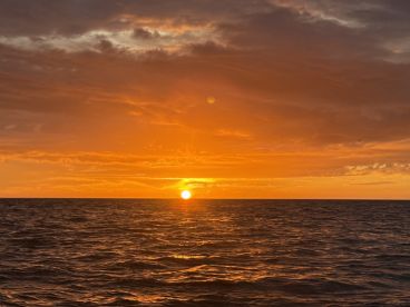A stunning sunset over the ocean, casting vibrant orange hues across the sky and water — a perfect backdrop for romantic evenings or peaceful boat rides.