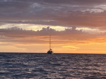 A serene sunset view featuring a sailboat in the distance, creating a picturesque scene on the open water — perfect for tranquil evening cruises.