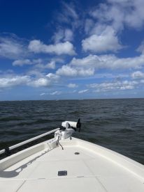 A clear view of the front deck of a boat cutting through the water, with a beautiful blue sky and clouds overhead, perfect for showcasing boating adventures.
