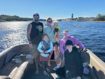 A joyful family poses together on a boat with a lighthouse in the background, capturing a memorable day on the water.